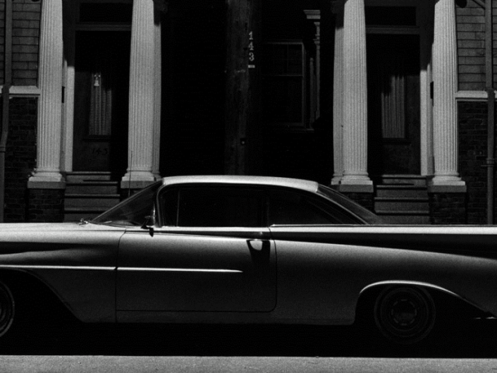 Black and white photograph from series Houses at Night by William Gedney of luxury old car near the sidewalk. Profile shot.