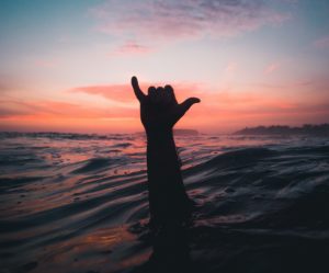 Person lifting his hand from the water in sunset background